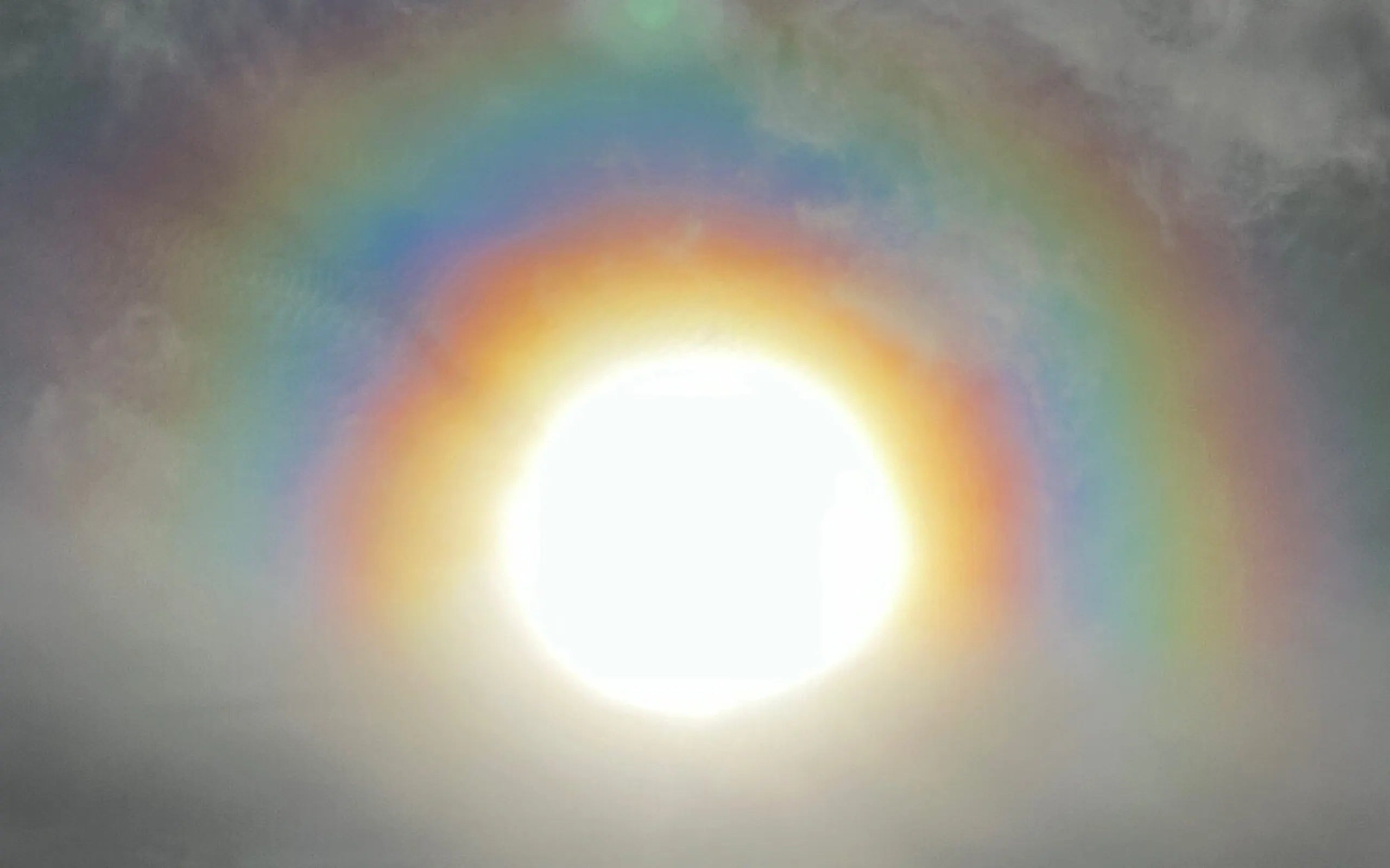 The sun ringed by a rainbow halo in a soft cloudy sky