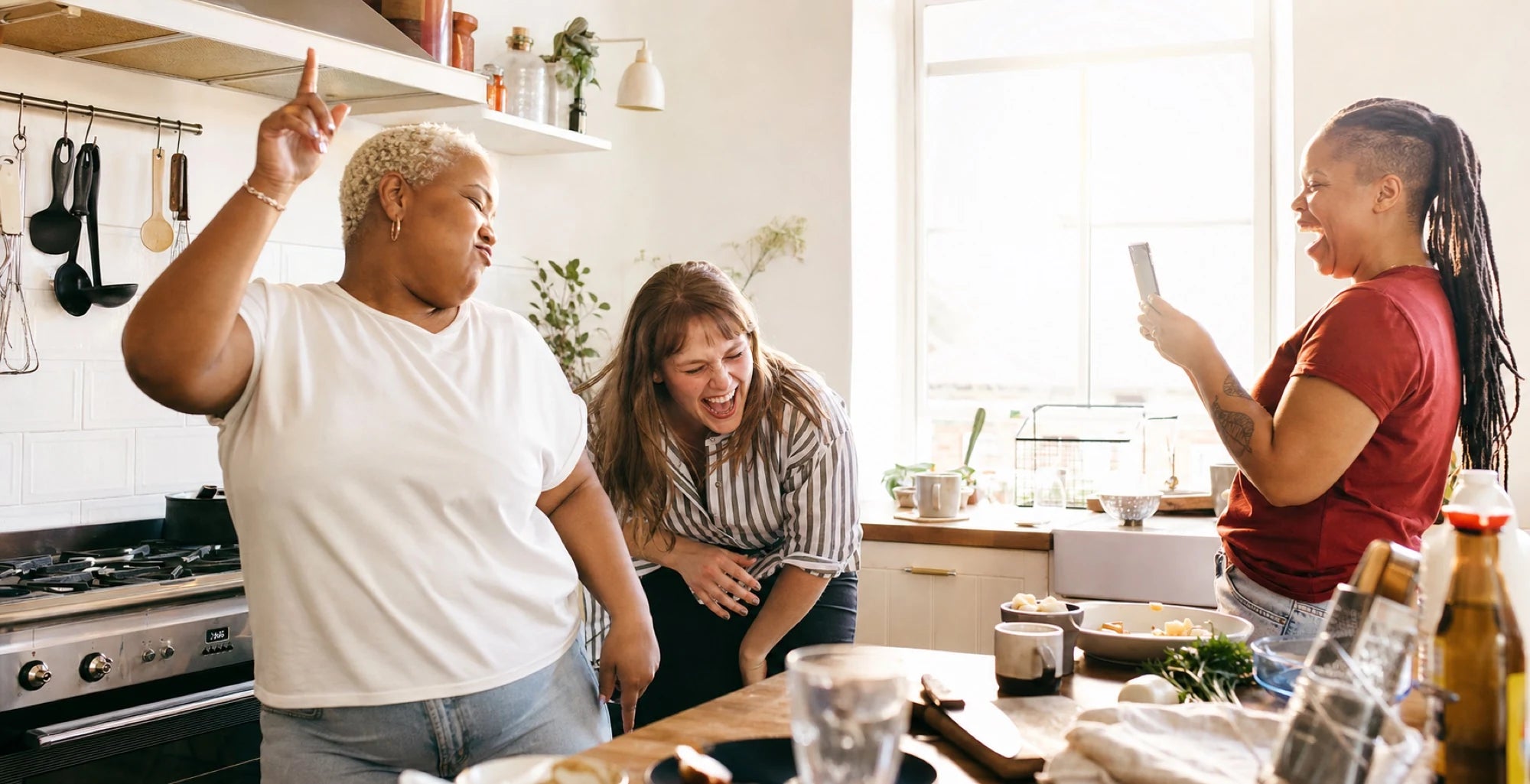 Three friends laughing together in a kitchen